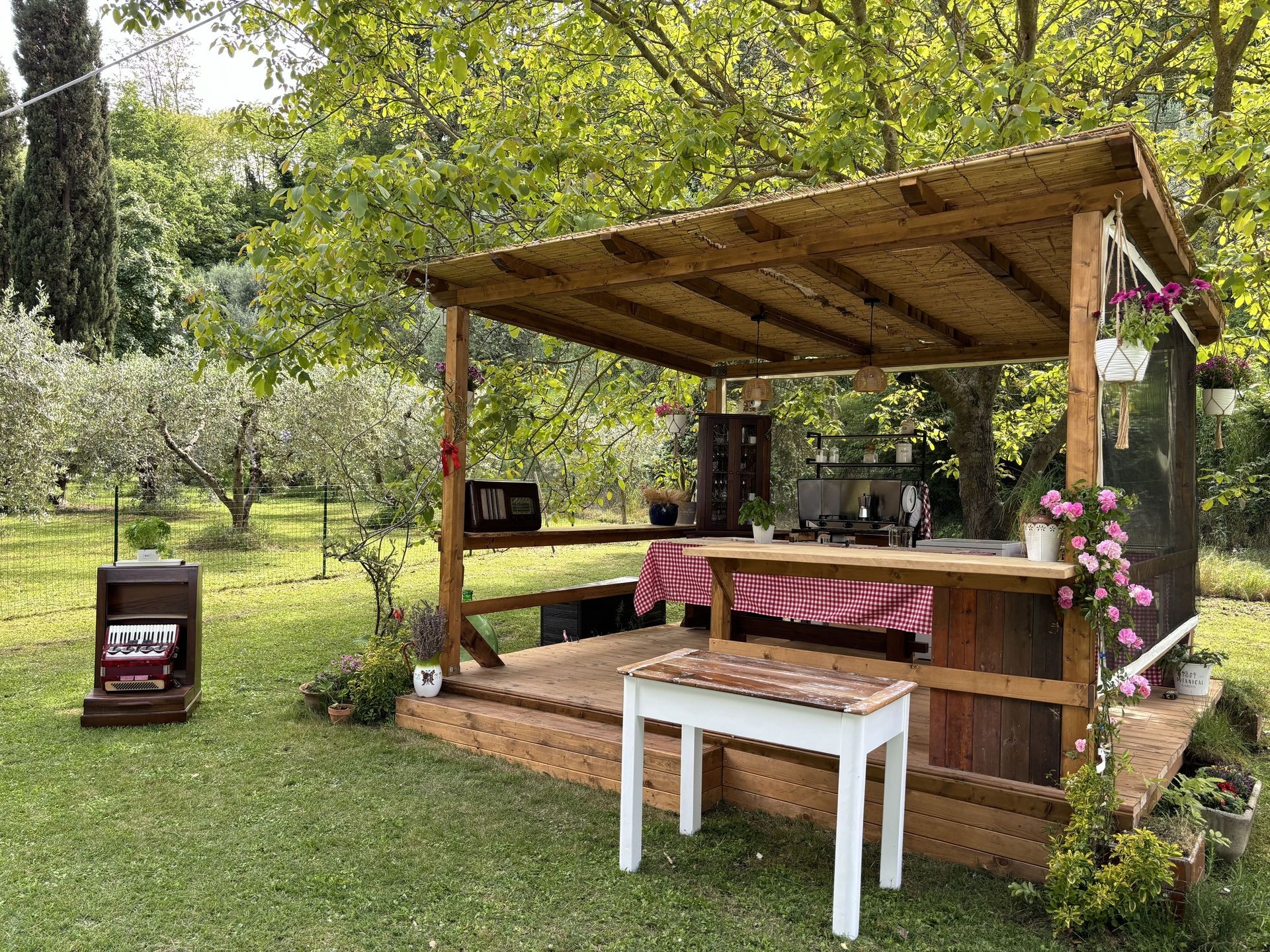 Outdoor wooden bar with a coffee machine, surrounded by trees and plants.